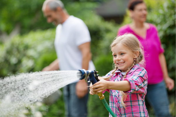 Glückliches Kind beim Garten gießen mit Wasser aus der Regenwasserzisterne