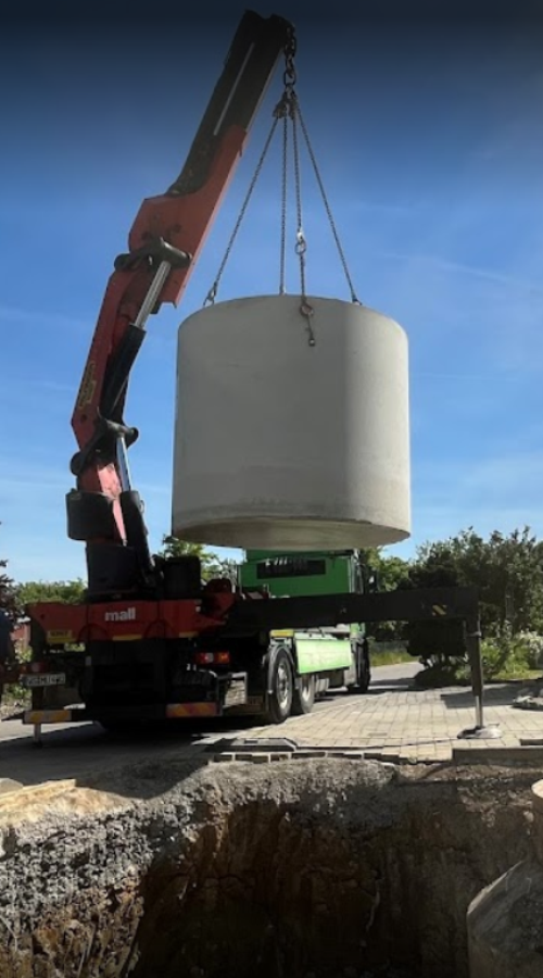 Auf dem Bild sieht man einen LKW der gerade einen Abwasser Anlage in ein vorbereitetes Loch setzt für die Abwassersammlung